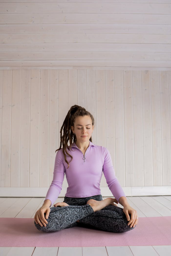 services-01 Woman practicing yoga meditation indoors on a pink mat, focusing on relaxation and mindfulness.